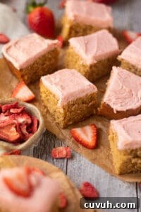 side angle shot of sliced peanut butter cake with strawberry frosting on a wooden cutting board. sliced strawberries scattered in perimeter of shot.
