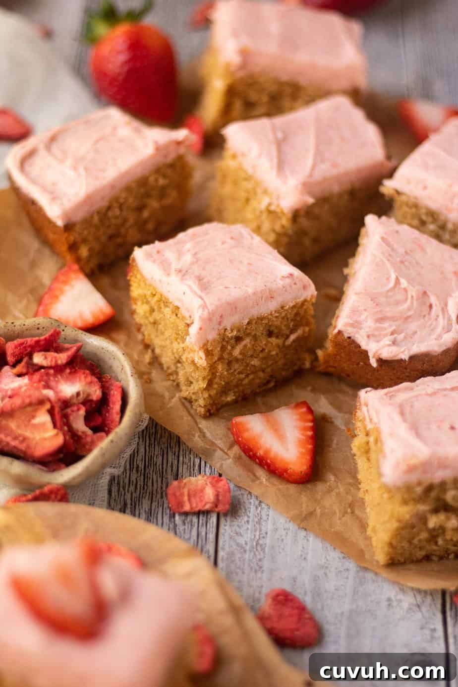 Peanut Butter Layer Cake with Strawberry Buttercream Frosting 4 side angle shot of sliced peanut butter cake with strawberry frosting on a wooden cutting board. sliced strawberries scattered in perimeter of shot.