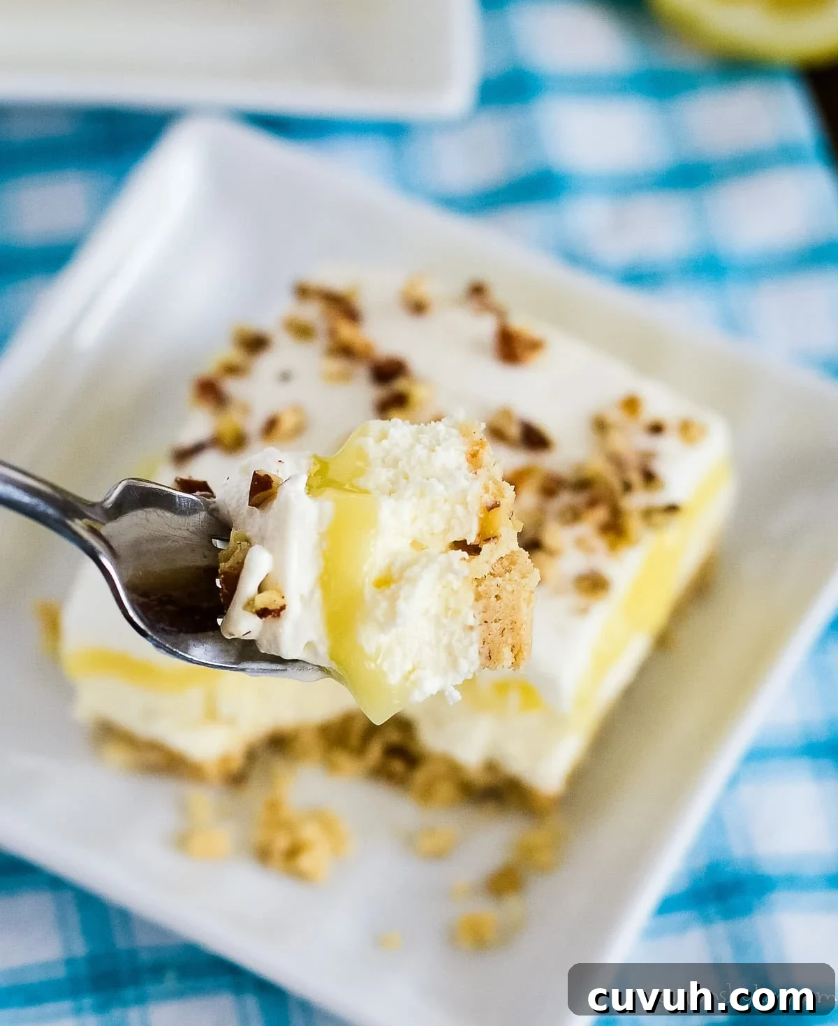 bite of lemon lush on a fork with a plate of dessert underneath