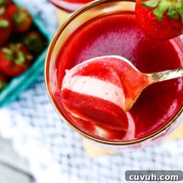 Layered strawberries and yogurt gelatin treat in a small cup with a spoon sticking out.