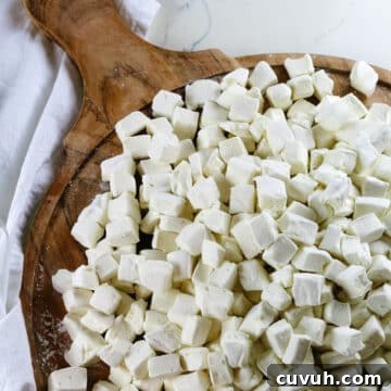 homemade marshmallows cut into bite-size pieces on a circular wooden cutting board.