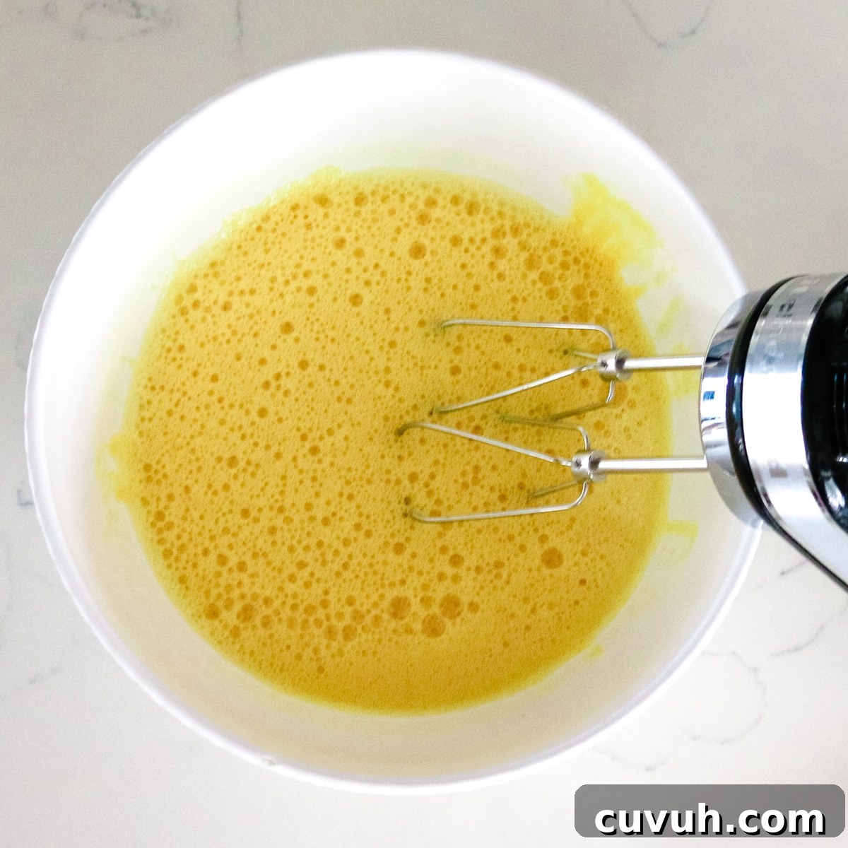Whisking the egg with a mixer in a white bowl.