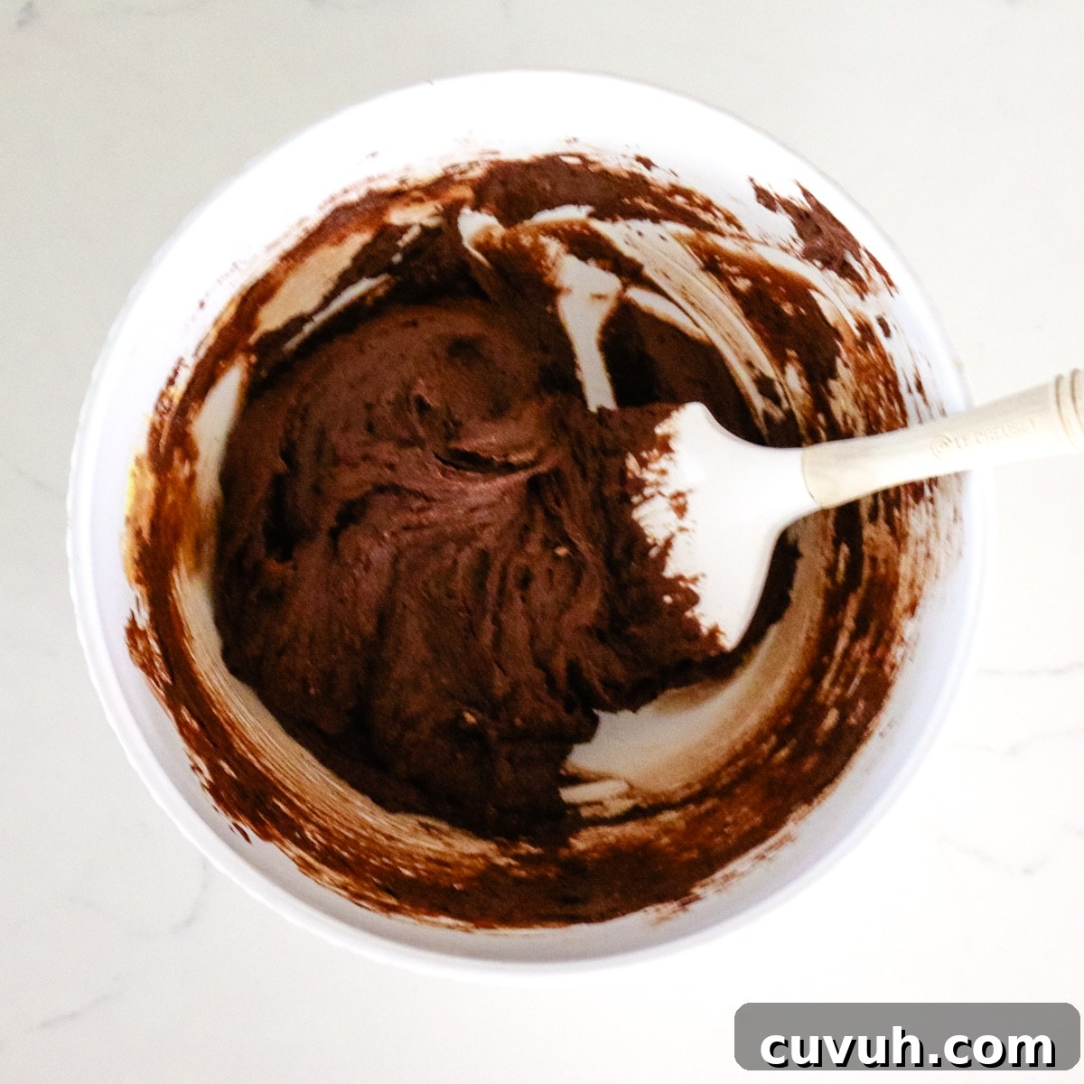 Mixed coconut flour in a white bowl with a spatula in it.