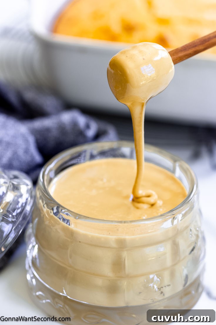 A wooden honey dipper is pouring whipped honey into a glass honey jar