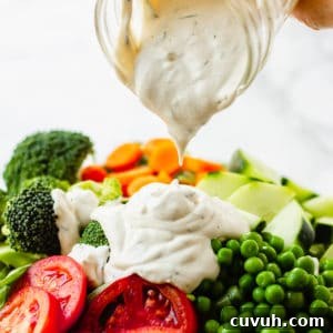 pouring vegan ranch dressing over a large green salad.