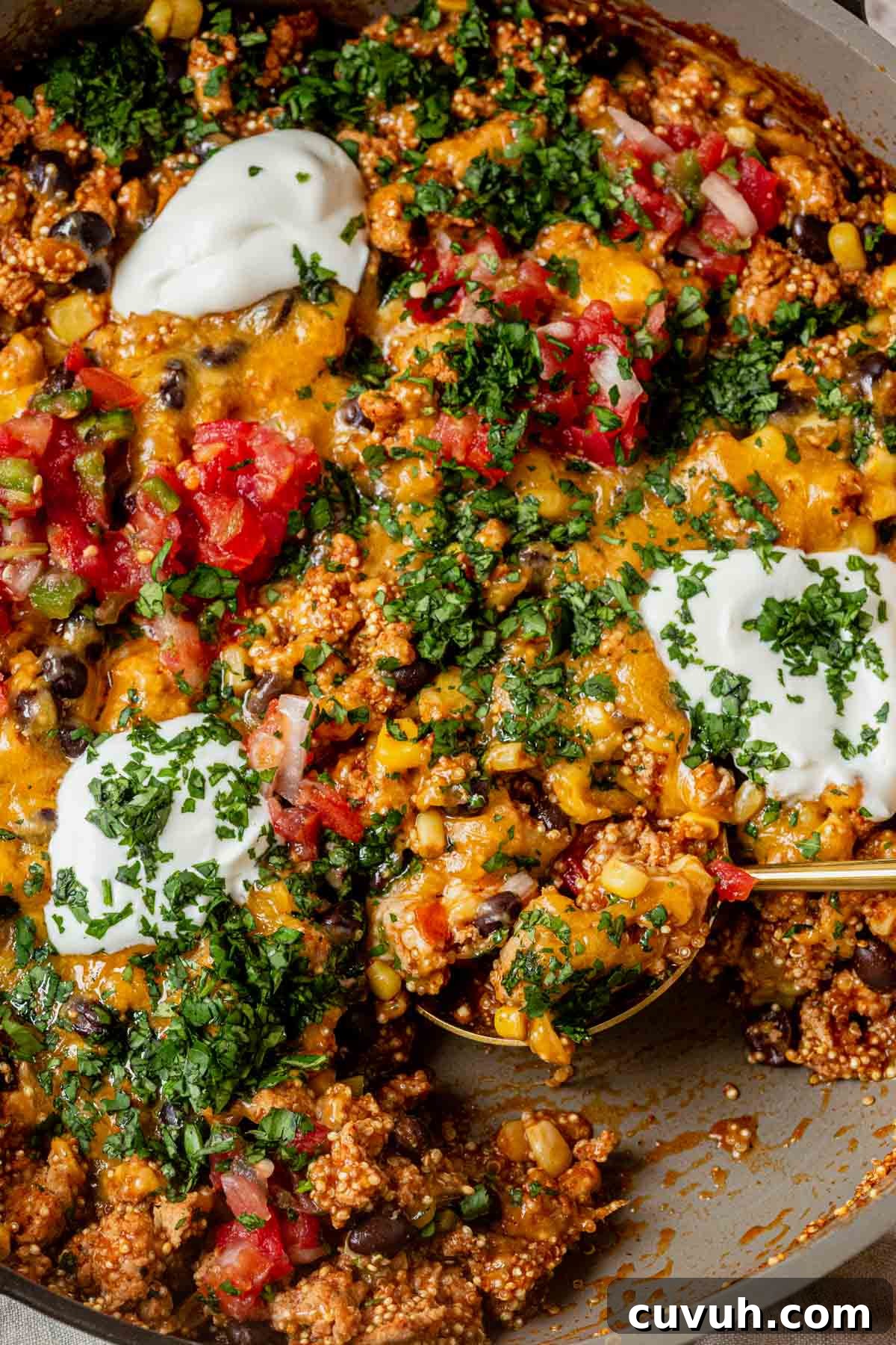 enchilada quinoa skillet topped with sour cream and cilantro with a spoon scooping a portion out.