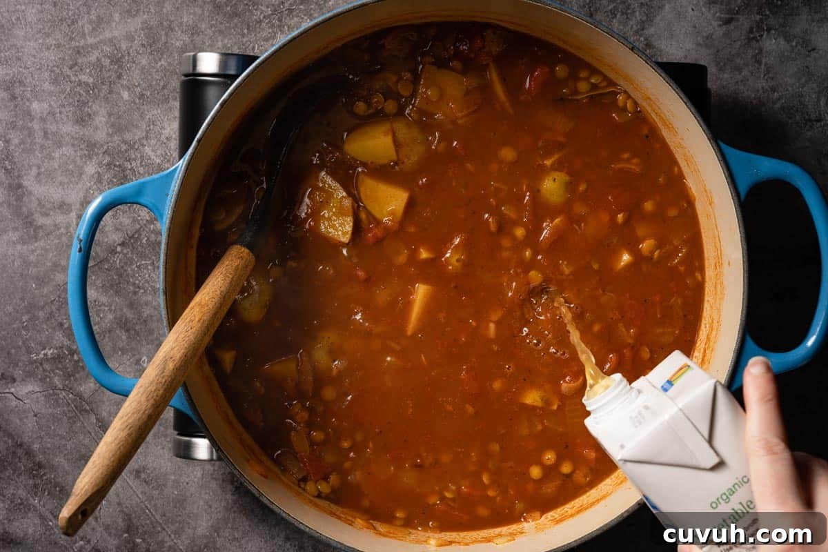 Hearty Lentil and Potato Soup Recipe for Comforting Weeknight Meals 13 broth being poured into soup cooking in blue pot