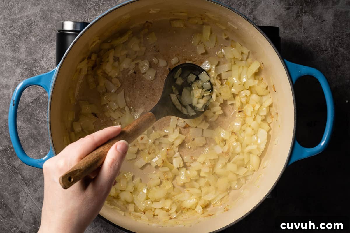 Hearty Lentil and Potato Soup Recipe for Comforting Weeknight Meals 8 onion cooking in pot and being stirred with spoon