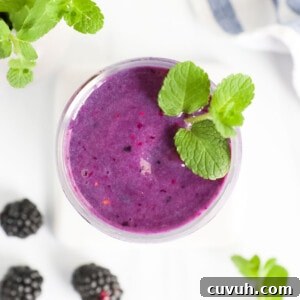 An overhead image of a bright purple smoothie in a clear cup with fresh mint on top.