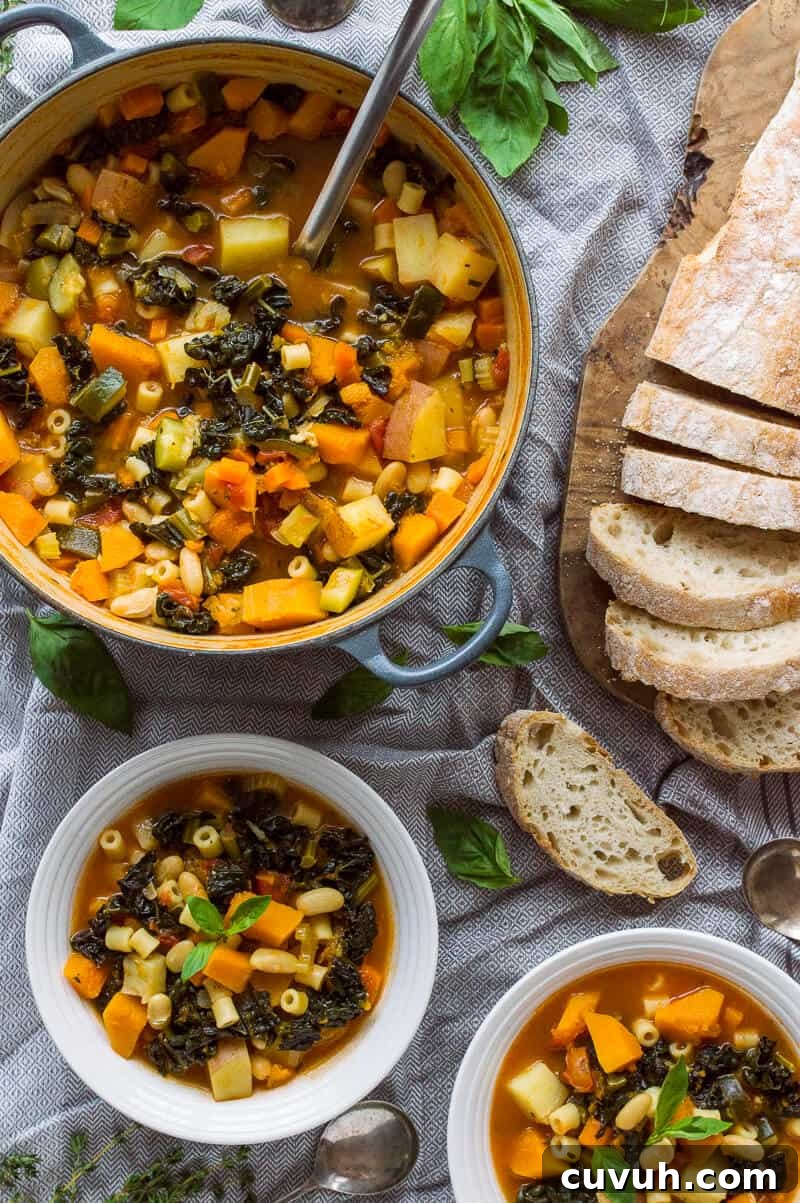 Autumn Vegan Minestrone Soup with Seasonal Vegetables 4 A pan of vegan autumn minestrone soup with two bowlfuls and sliced ciabatta on a grey tablecloth.