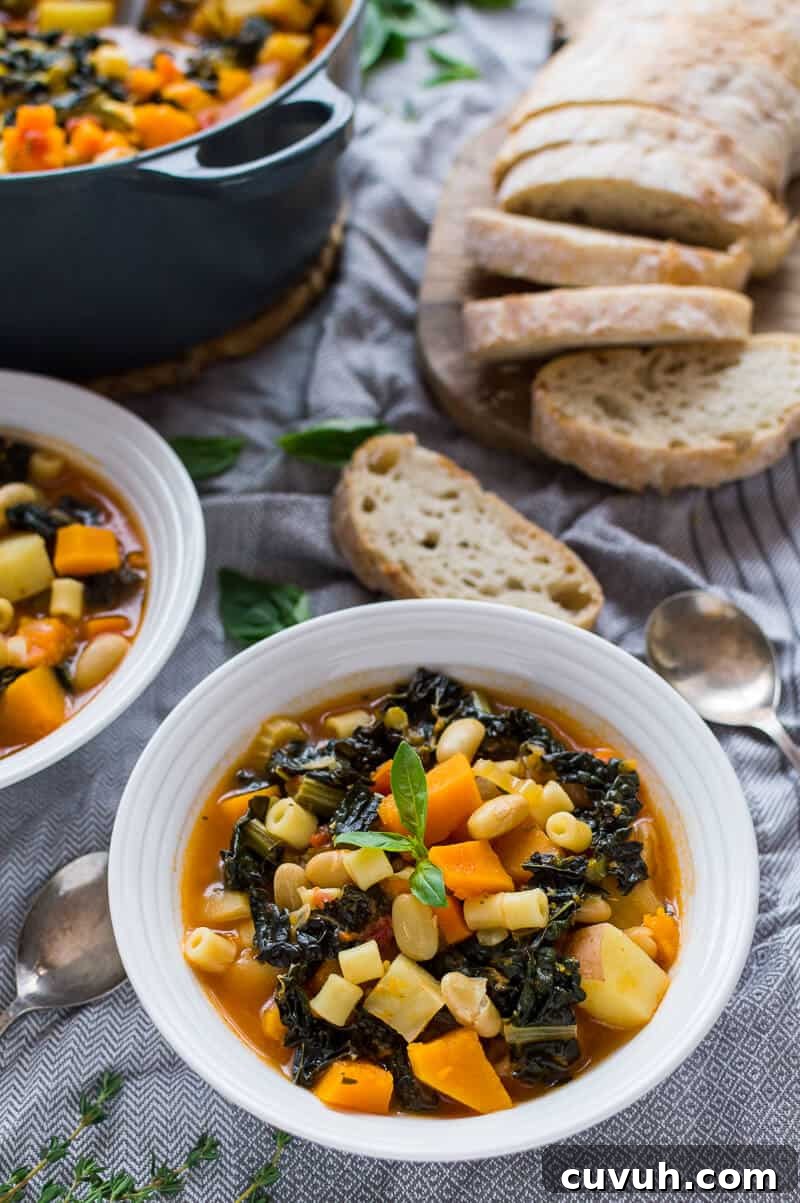 Autumn Vegan Minestrone Soup with Seasonal Vegetables 8 A bowl of Autumn minestrone soup on a grey tablecloth with ciabatta and a pan of soup in the background.