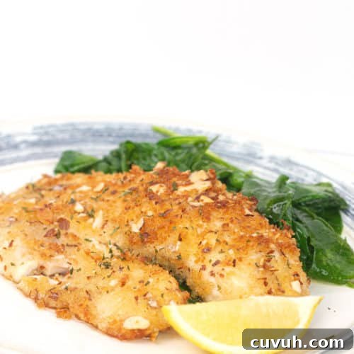 white and blue plate with almond crusted tilapia with a lemon slice and spinach