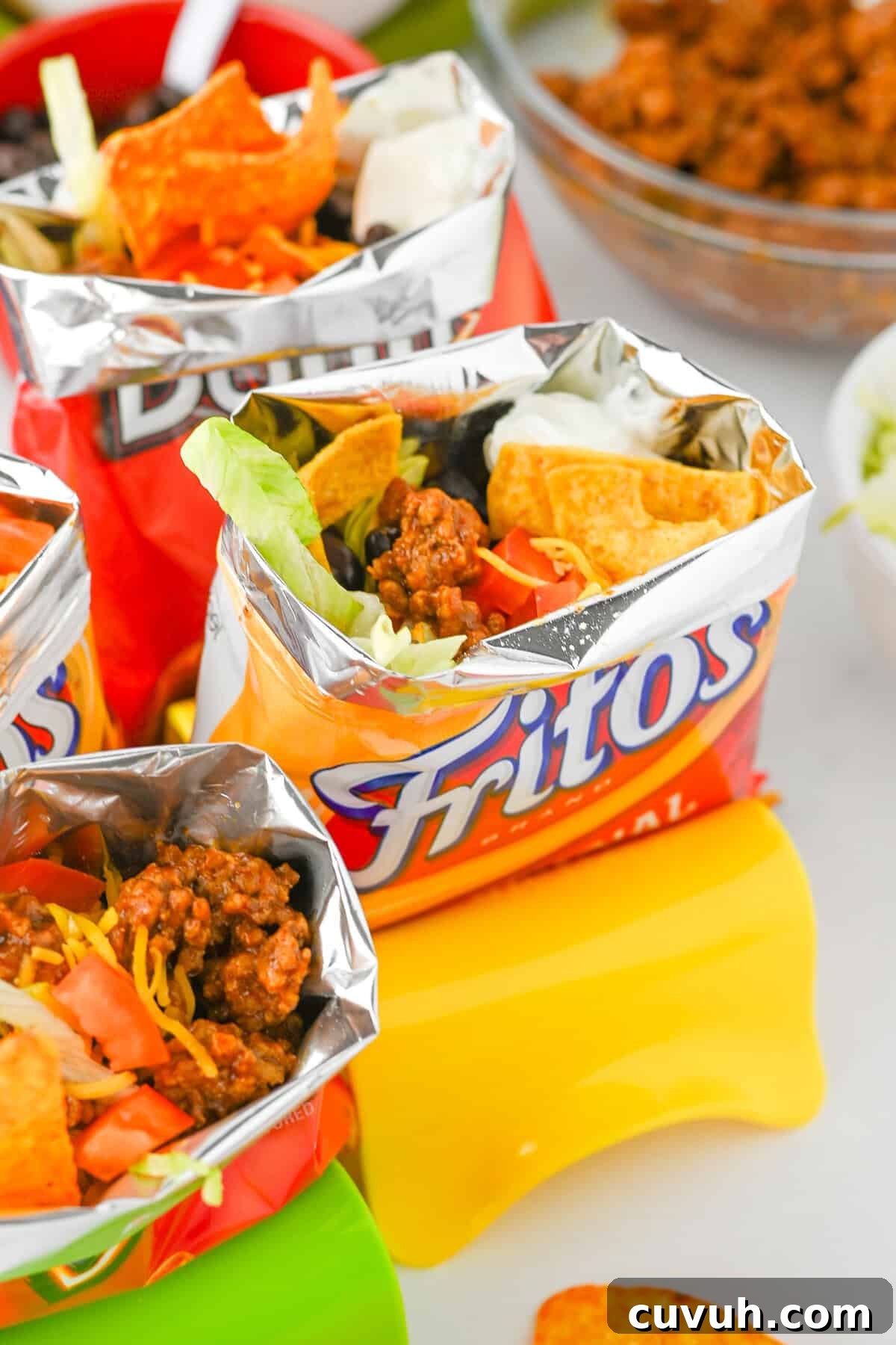 How to Make Walking Tacos: Quick Party-Friendly Recipe 2 Fritos walking taco in focus with toppings like shredded cheese, beans, sour cream, and lettuce.