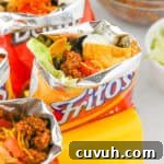 How to Make Walking Tacos: Quick Party-Friendly Recipe 8 Fritos walking tacos with toppings like shredded cheese, beans, sour cream, and lettuce.