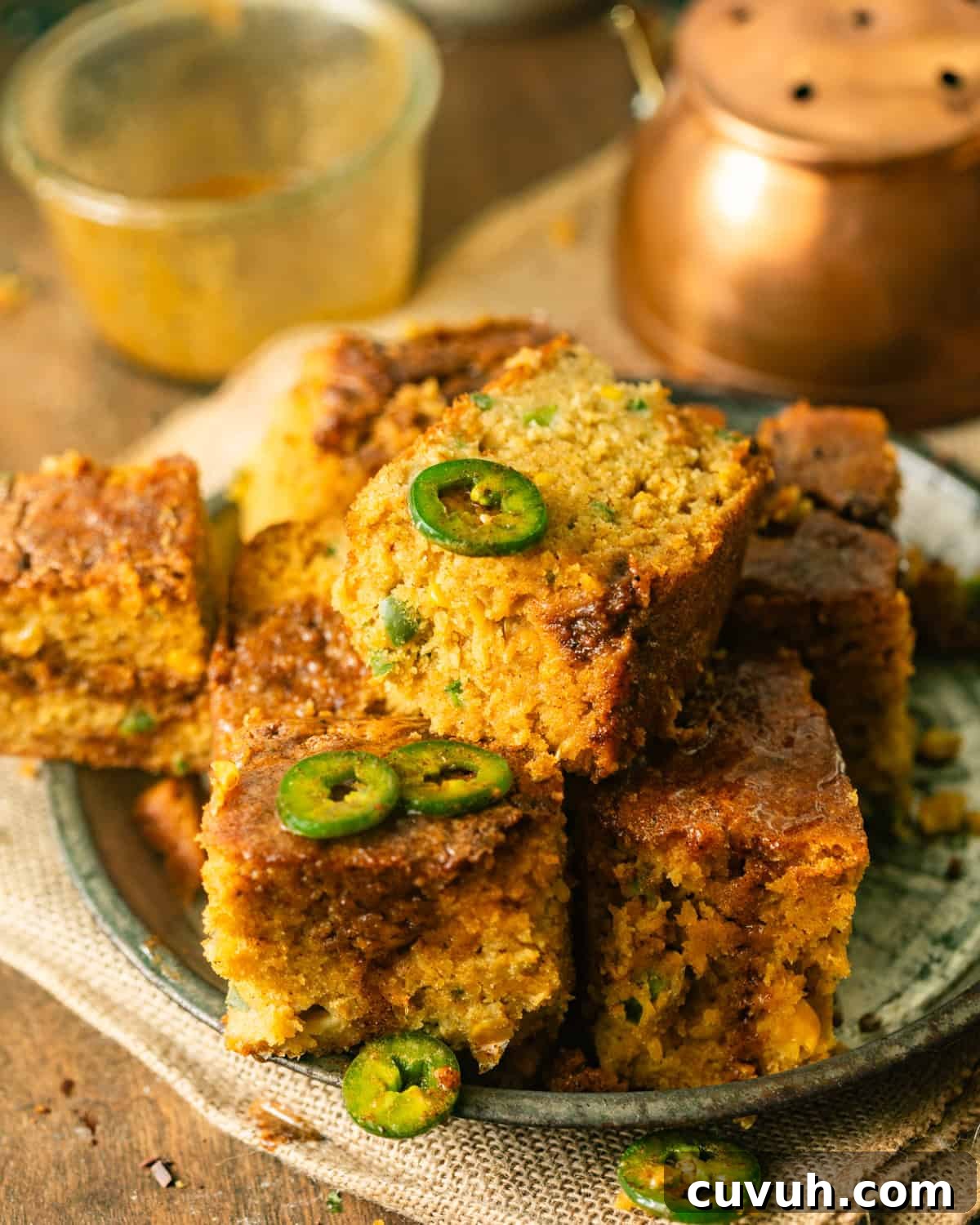 Spicy Jalapeño Honey Cornbread Recipe 3 sliced pieces of jalapeno cornbread on a serving plate topped with fresh jalapenos and honey butter.