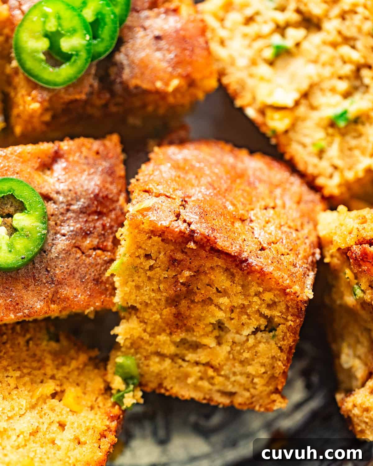 Spicy Jalapeño Honey Cornbread Recipe 10 sliced honey jalapeno cornbread on a pie plate with honey butter and jalapenos on top.