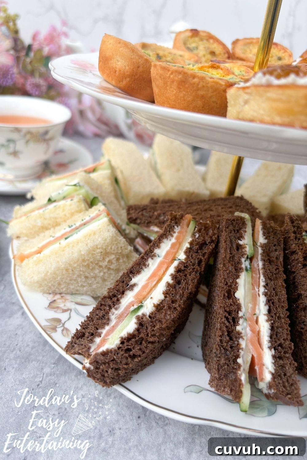 Smoked Salmon Tea Sandwiches with Cream Cheese, Cucumber & Dill 3 Smoked salmon tea sandwiches with cream cheese, cucumber, and dill on a plate with mini quiches and crostini, served alongside floral china tea cups and a matching teapot for an afternoon tea party.