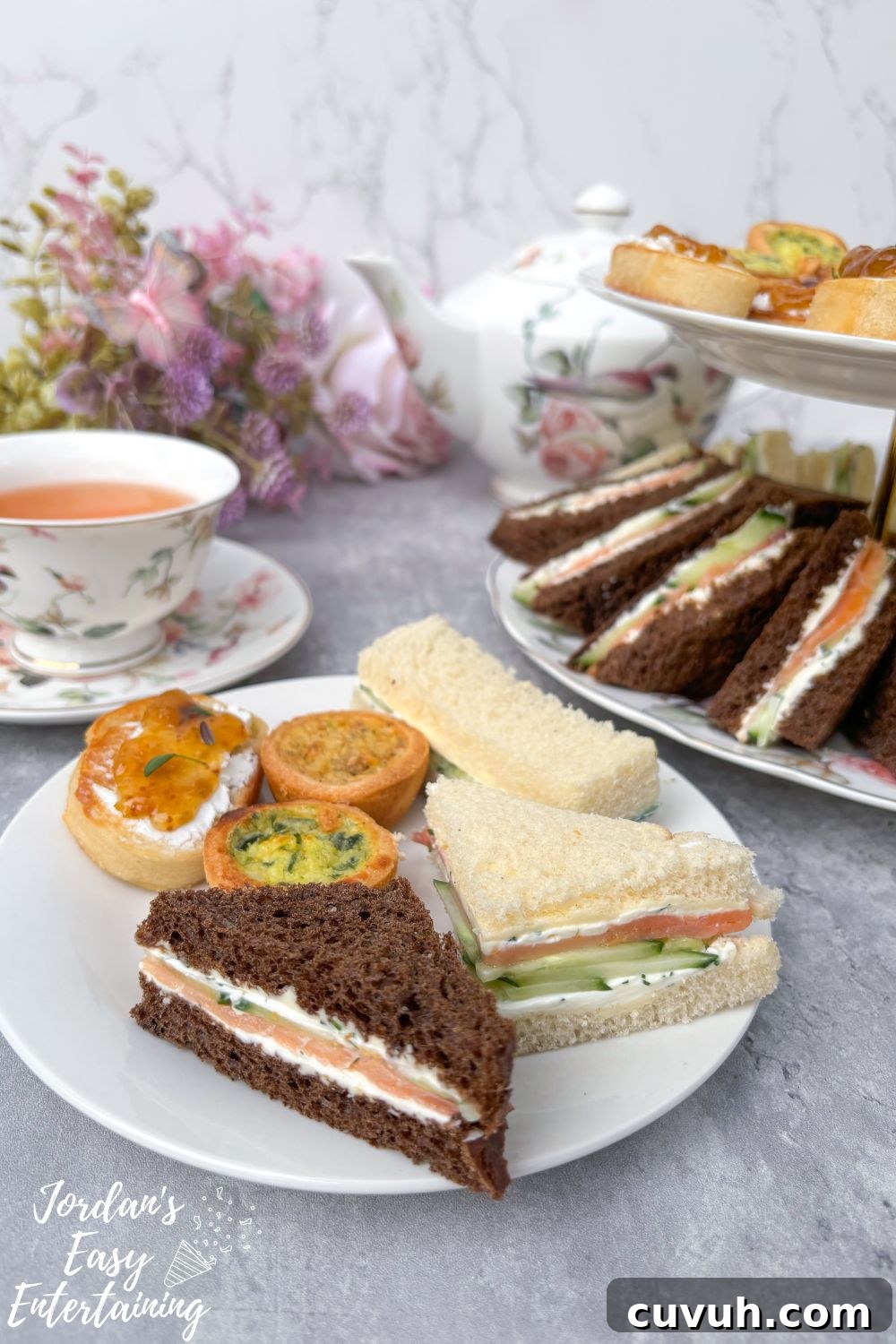 Smoked Salmon Tea Sandwiches with Cream Cheese, Cucumber & Dill 6 Smoked salmon tea sandwiches with cream cheese, cucumber, and dill on a plate with mini quiches and crostini, served alongside floral china tea cups and a matching teapot for an afternoon tea party.