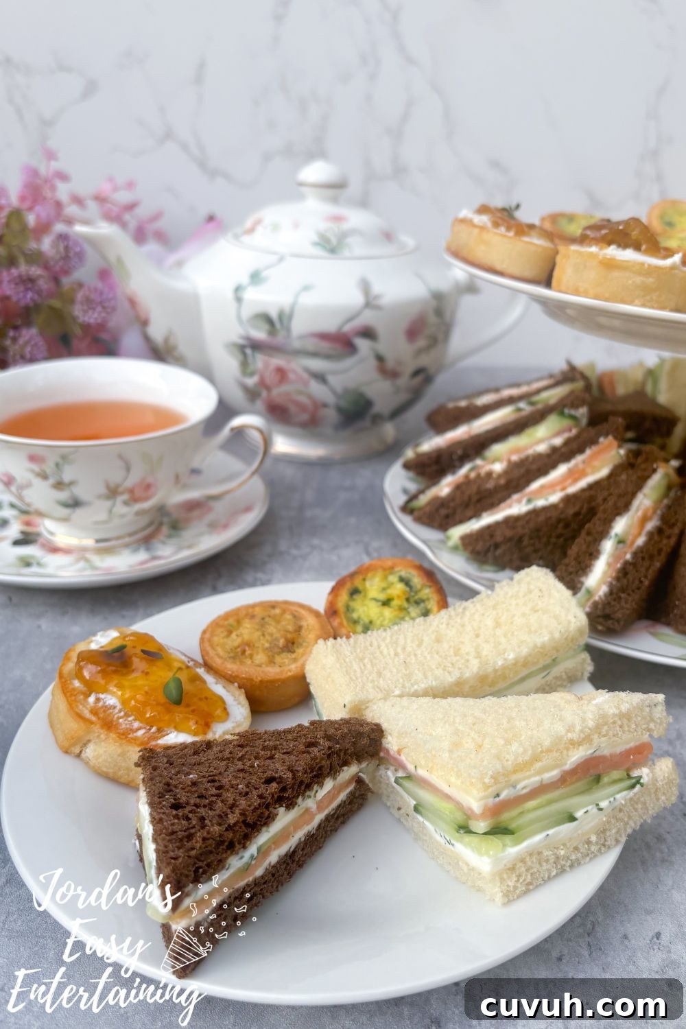 Smoked Salmon Tea Sandwiches with Cream Cheese, Cucumber & Dill 7 Smoked salmon tea sandwiches with cream cheese, cucumber, and dill on a plate with mini quiches and crostini, served alongside floral china tea cups and a matching teapot for an afternoon tea party.