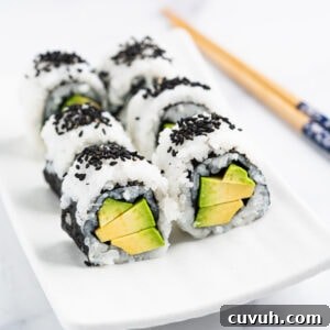 Sushi roll stuffed with creamy avocado standing up on a plate topped with black sesame seeds.