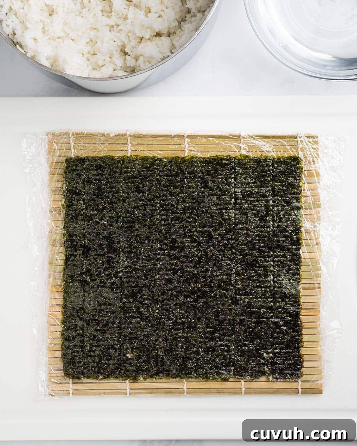 Nori seaweed sheet on top of bamboo sushi mat covered with plastic wrap.