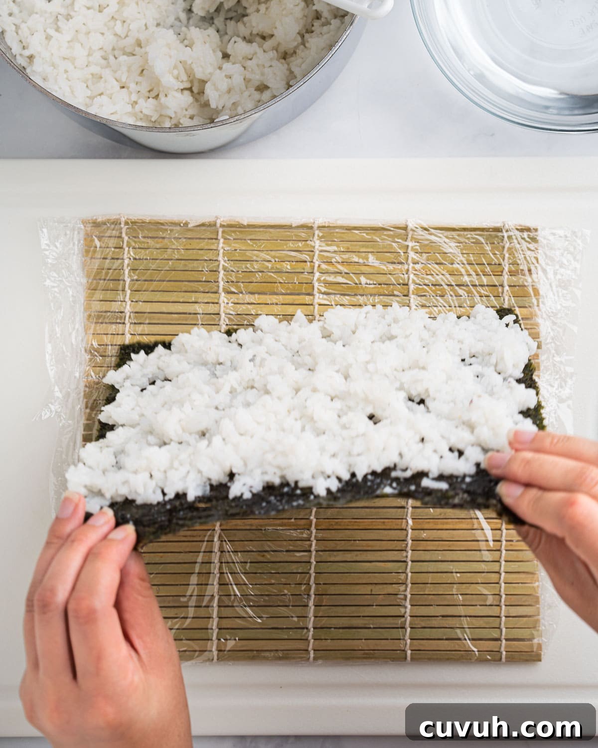 Hands flipping nori sheet covered with rice over to face down.