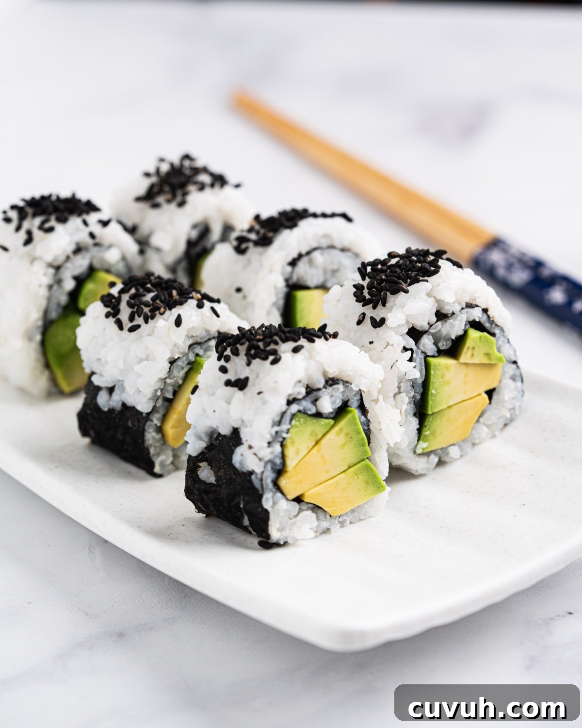side view of avocado rolls standing up on a plate with chopsticks in the background.