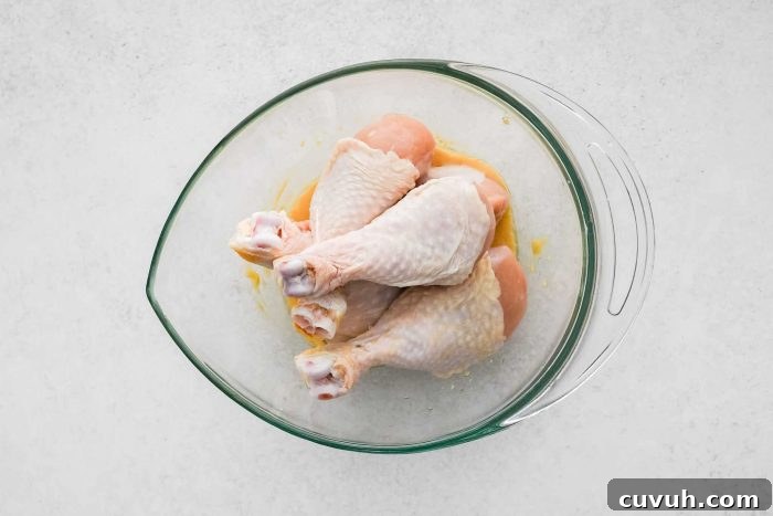 Crispy Shake-and-Bake Chicken Recipe for Perfect Weeknight Meals 6 Large glass mixing bowl filled with chicken drumsticks set on top of melted butter and Dijon mustard.