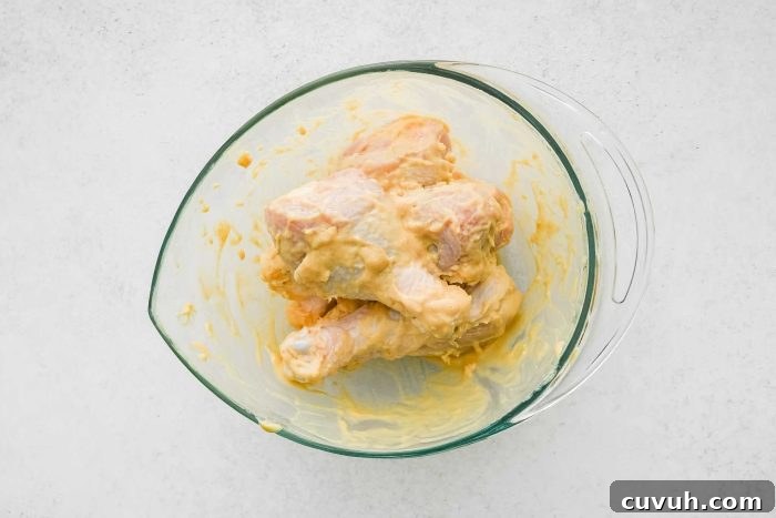 Crispy Shake-and-Bake Chicken Recipe for Perfect Weeknight Meals 7 Large glass mixing bowl filled with chicken drumsticks coated in melted butter and Dijon mustard.
