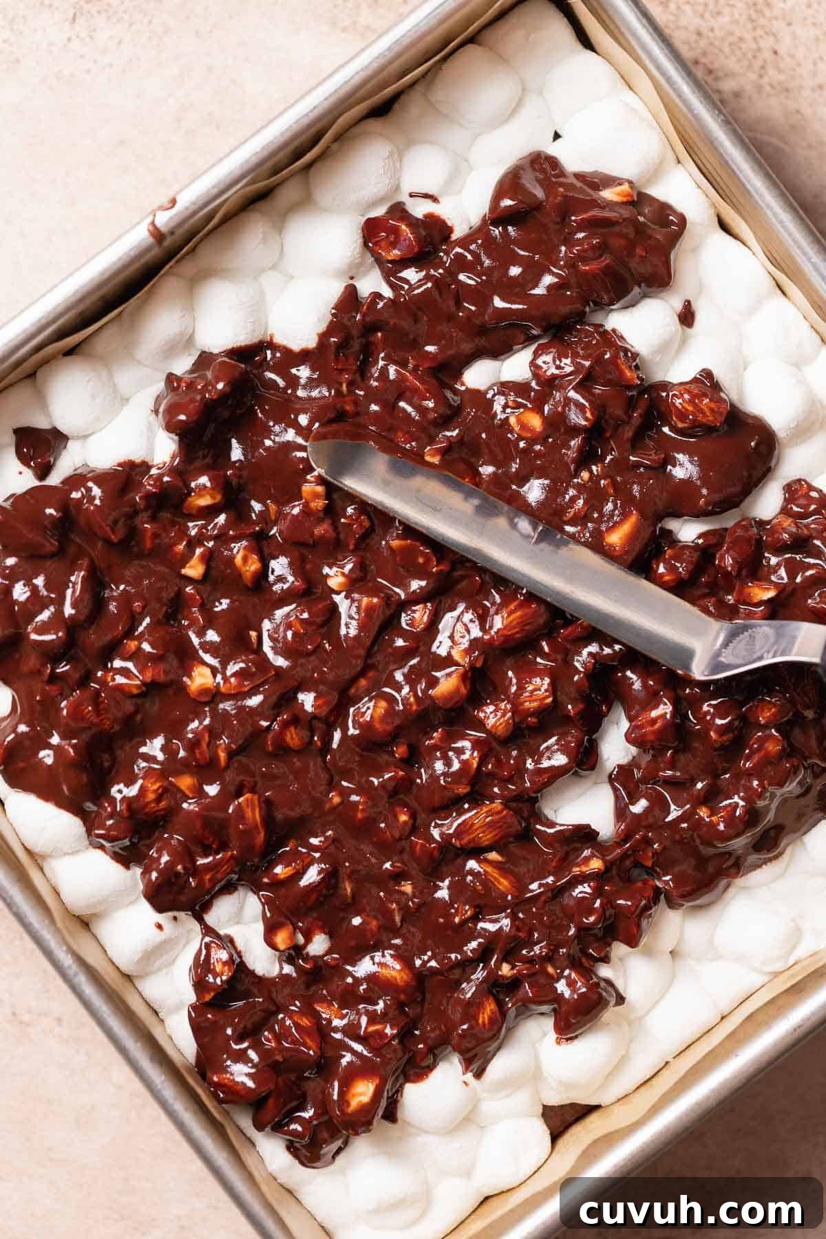 The almond ganache being spread on top of the puffy marshmallow layer.