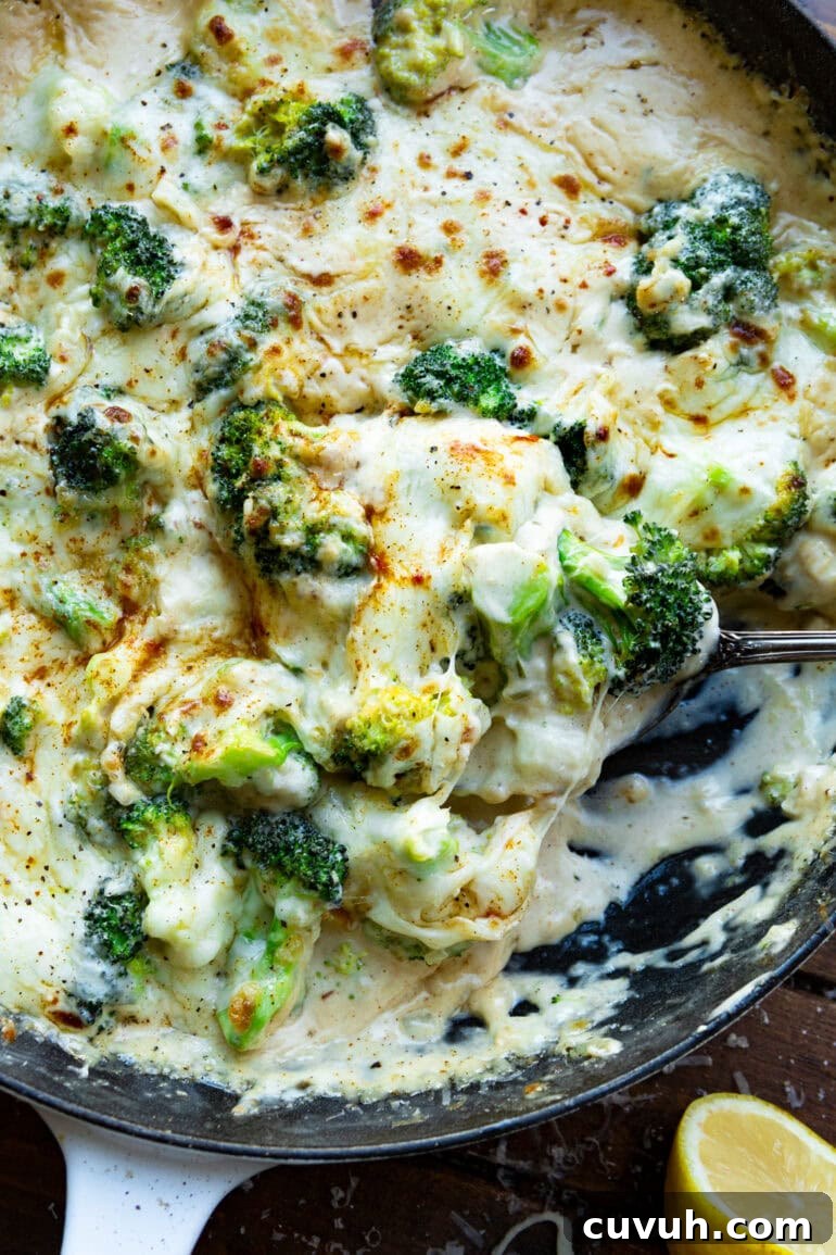 a photo of someone scooping up a serving of creamy parmesan garlic broccoli from a large skillet