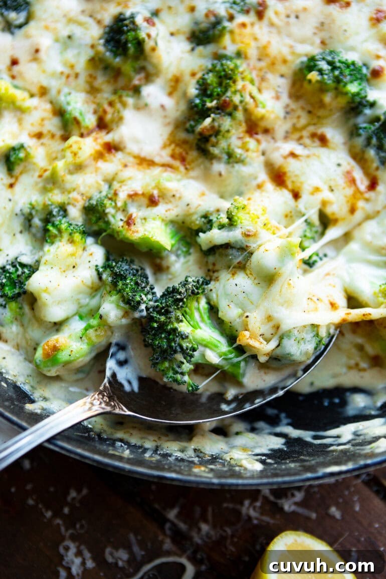 a photo of a skillet full of creamy garlic parmesan broccoli being scooped up by a large silver spoon