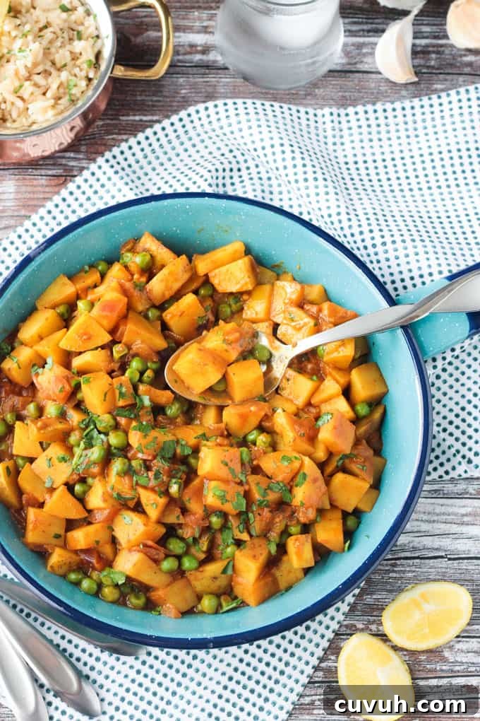 Potato and pea curry topped with cilantro in a blue skillet with a metal serving spoon resting on the side.