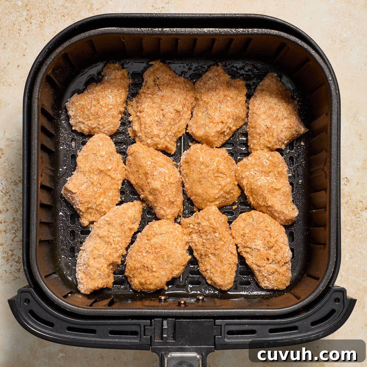 Tops of chicken sprayed with oil in air fryer basket.