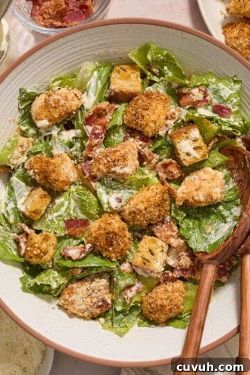 Air fryer chicken caesar salad served in a bowl with wooden serving spoons.