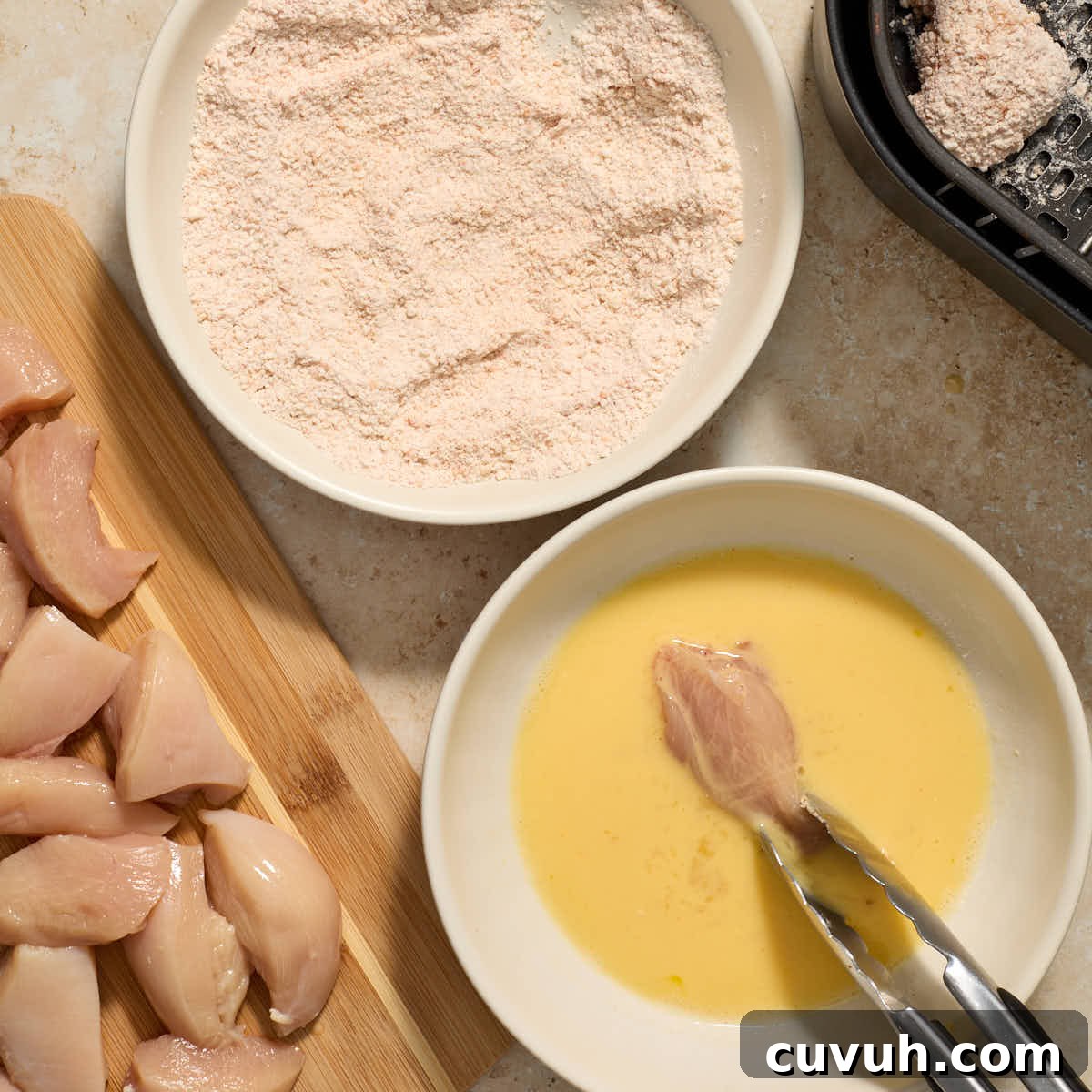 A piece of chicken being dipped in the egg mixture.