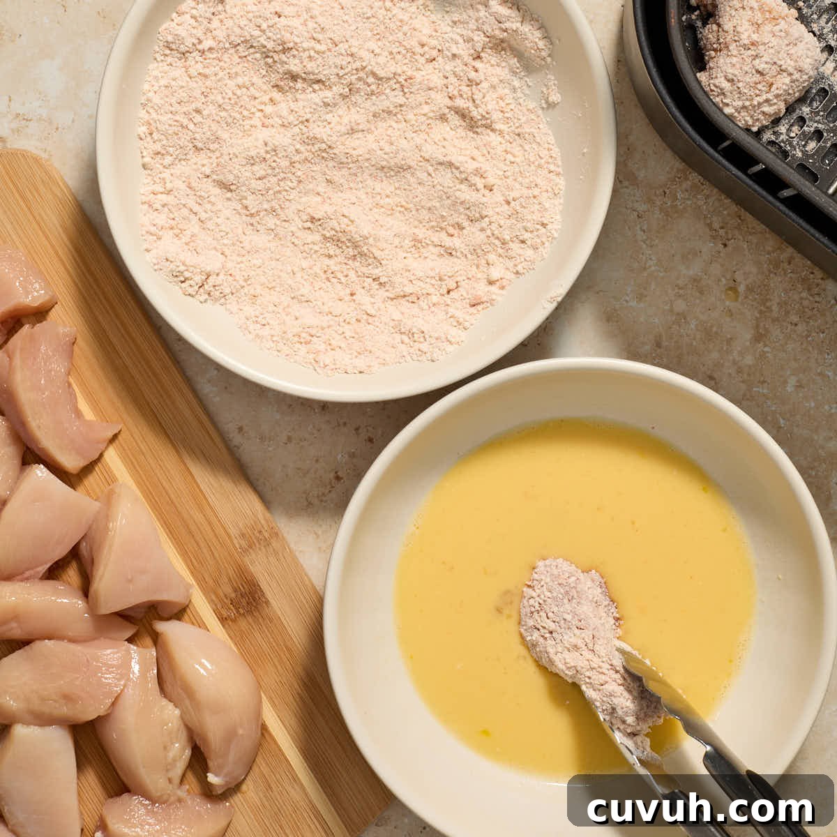 Piece of floured chicken being dipped in egg again.