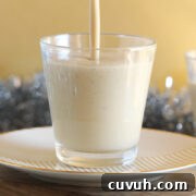 Pouring eggnog into a clear glass on a plate.