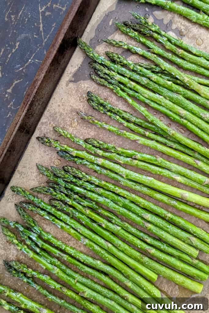 A sheet tray with brown parchment paper and on top is vibrant green roasted asparagus.