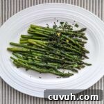 Overhead shot of fresh, green roasted asparagus topped with mint gremolata on a white platter. The platter sits on a tray striped tablecloth.