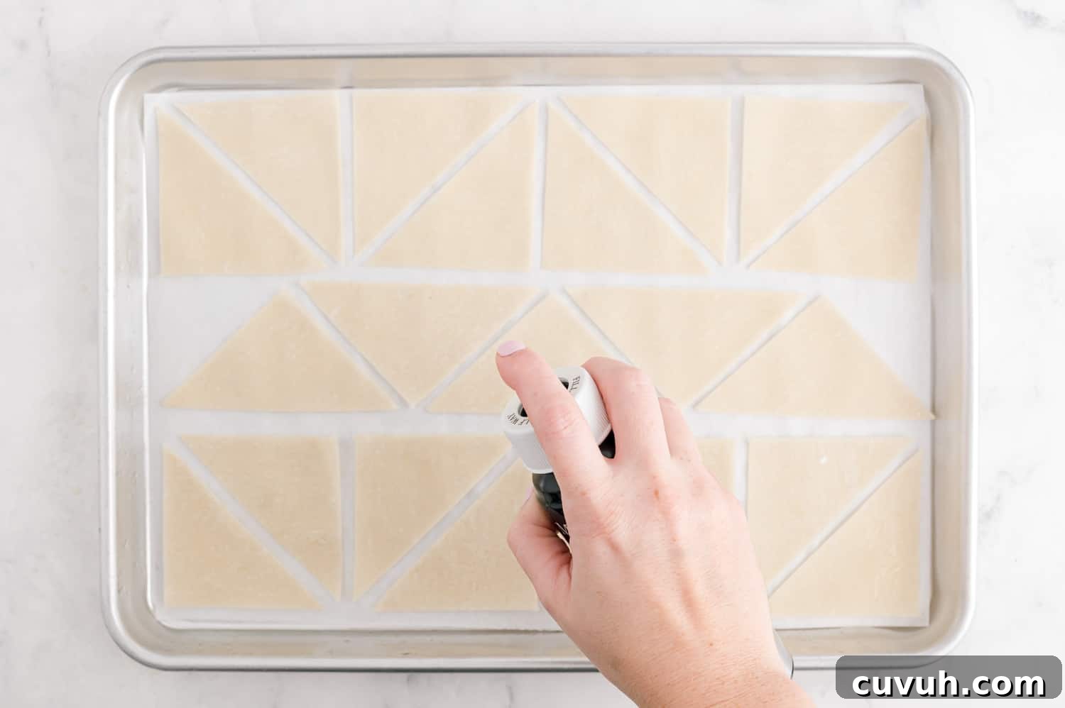 Wonton wrappers being sprayed with oil on a sheet pan.