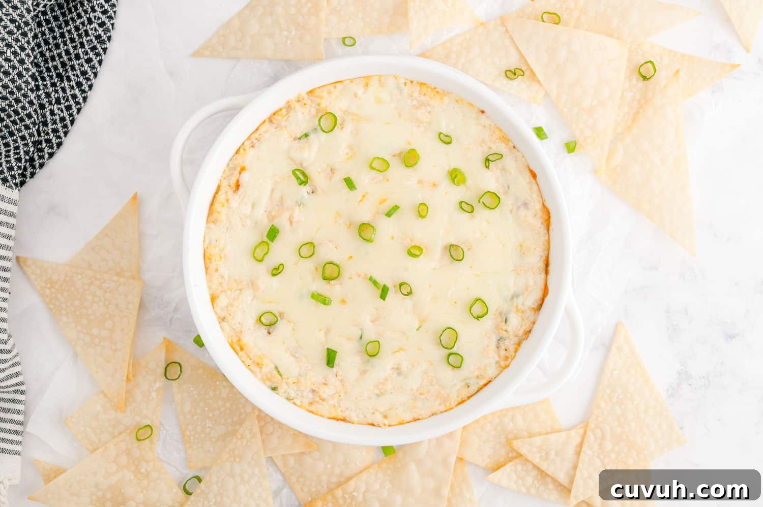 Dip, garnished with green onions, surrounded by wonton triangles.