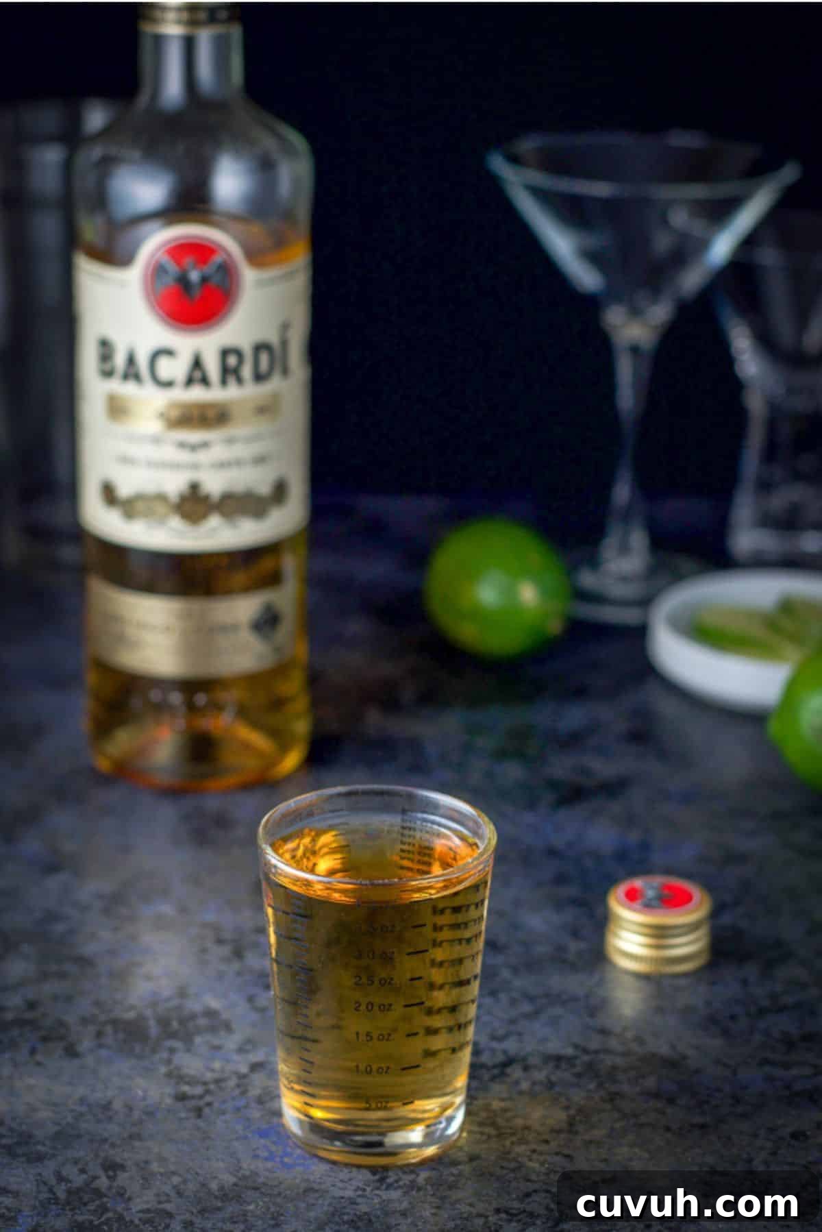 Gold rum measured out with the bottle behind it along with some glasses and lime