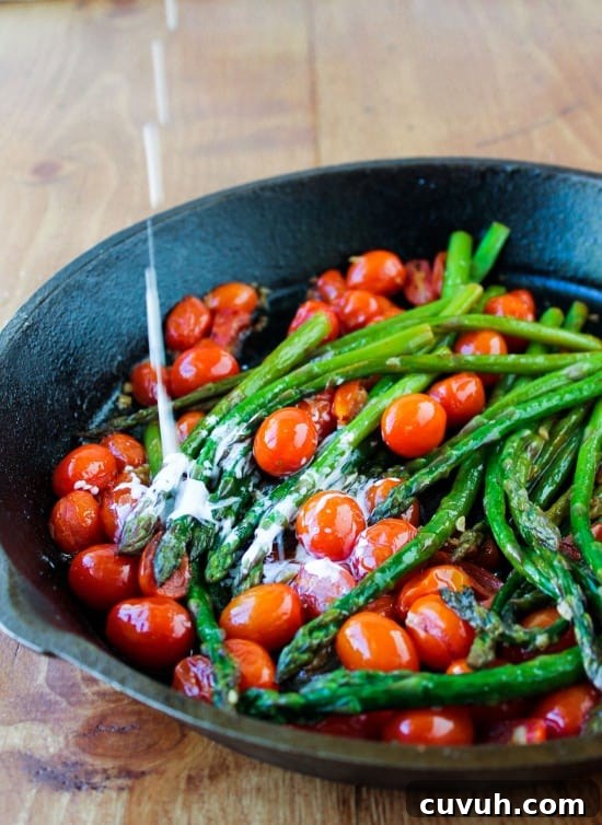 cream dripping into a cast iron pan of asparagus and cherry tomatoes.
