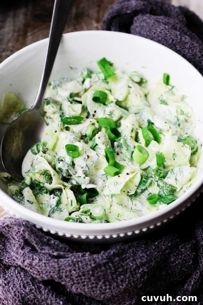 Polish cucumber salad - mizeria in a bowl with spoon in it and towel around it
