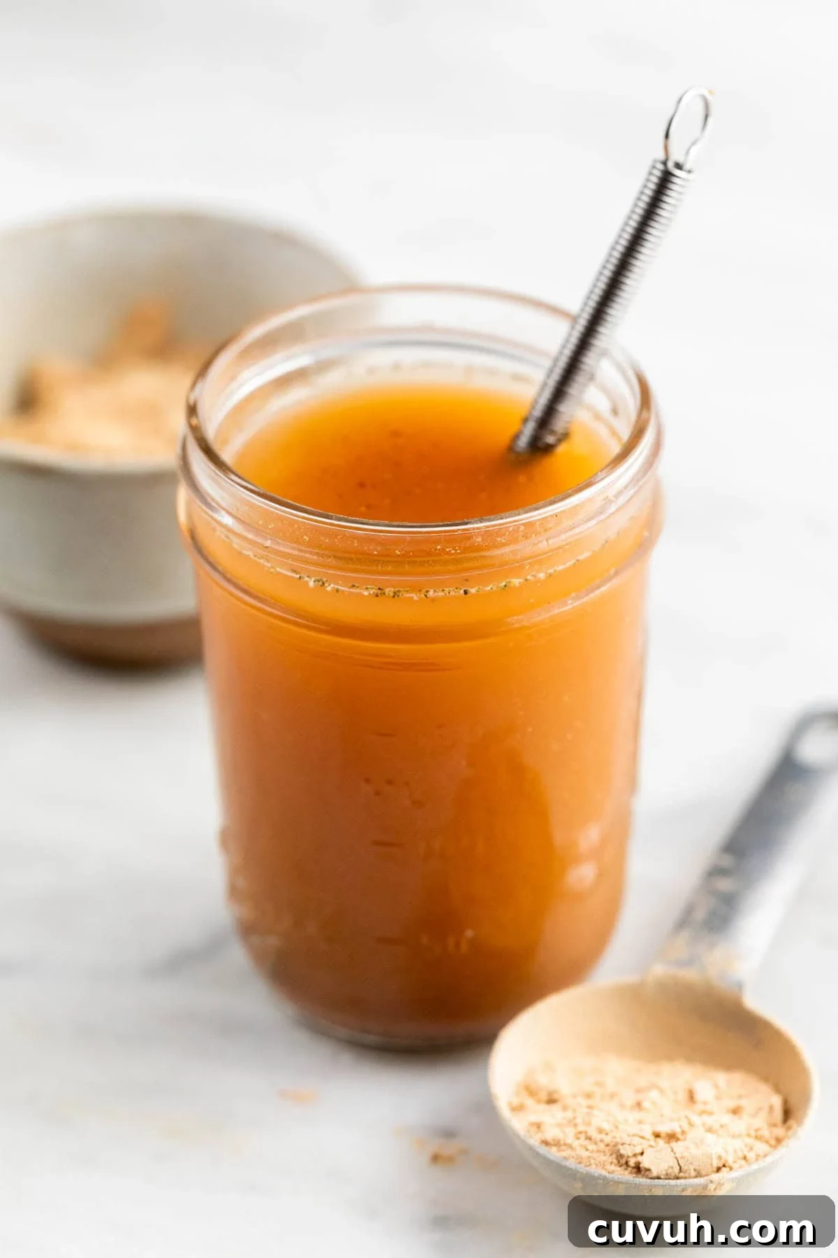 Vegan beef broth in a jar and vegan beef bouillon powder on a spoon.