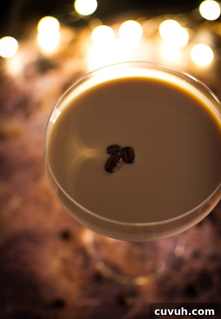 side angle of a martini glass holding a Brazilian coffee cocktail (batida de cafe) garnished with three coffee beans on a stone surface near a fire
